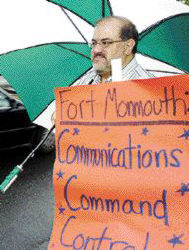 CHRIS KELLY staff Protesters like Jim Cafiero (l) took refuge under umbrellas as they stood outside Fort Monmouth in the early morning rain June 3, awaiting the arrival of BRAC commissioners. 