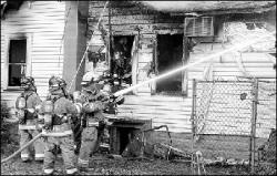 PHOTOS BY RYAN D. FENSTERMAKER  Above, firefighters shoot water onto a house on Spotswood-Englishtown Road in Monroe Sunday. Two residents were injured in the blaze, and the house was destroyed.  Left, firefighters work at the rear of the house.