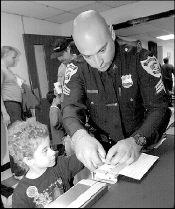 CHRIS KELLY Spotswood Police Sgt. Joseph Seylaz (above) fingerprints 5-year-old Danielle Hamilton of Spotswood during Family Day, held Sunday at Spotswood High School, Summerhill Road. Below, Dominick Bonacci, 7, of Spotswood, takes a turn on some simulated driving inside a replica of the car belonging to NASCAR&rsquo;s Jeff Burton at Family Day.