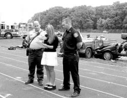 STEVEN M. BARON Kari Wasserman speaks after a mock DUI accident presented to the East Brunswick High School senior class June 3. She is flanked by police Lt. John D&rsquo;Antuono (l) and Capt. James Varick of the East Brunswick Independent Fire Company.
