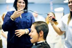  Teacher Kim Felicetta (l-r) watches as Vice Principal Myrna Velez has her head buzzed by cosmetology student Samantha Steneck, who won the right to cut Velez&rsquo;s hair off by raising the most money for cancer charity, the Family Reach Foundation. The three are part of the Cosmetology Program at the Monmouth County Vocational School in Hazlet, which hosted Operation: Bald Eagle on Feb. 13.  ERIC SUCAR staff 